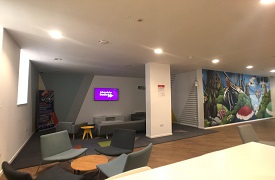 A large room with four armchairs around a small table, and two sofas and an armchair facing a television screen on the wall.