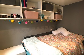 A room with a single bed and a set of shelves on the wall above it.