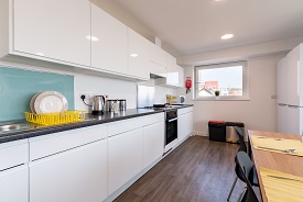 A kitchen with an oven and hob, a sink, two fridge freezers and several cupboards and drawers. There is a dining table nearby with two chairs next to it.
