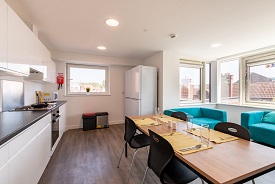 A kitchen with an oven and hob, two fridge freezers and several cupboards and drawers. There is a dining table in the centre of the room with four chairs around it, and two sofas nearby.