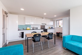 A kitchen with an oven and hob, a sink, a fridge freezer and several cupboards and drawers. There is a dining table in the centre of the room with four chairs around it.