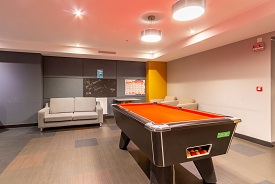 A room with a sofa, table and two armchairs against the walls, and a pool table in the centre.