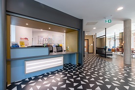 A large room with a reception counter and a seating area nearby with several sofas, chairs and tables.