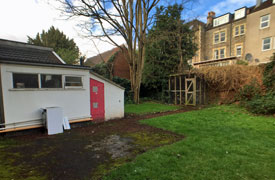 A walled garden with a grass and paved areas. There is a bike storage cage at the far end of the garden.