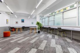 A large room with desks lining two walls, some chairs against the desks, and two other tables in the centre of the room.