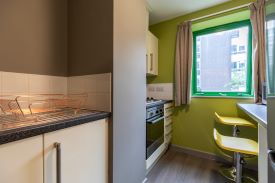 A kitchen with a counter and two chairs against one wall, and an oven and hob and several cupboards and drawers against the opposite wall.