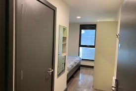 A bedroom with a single bed, wardrobe, wall mounted mirror and coat hooks.