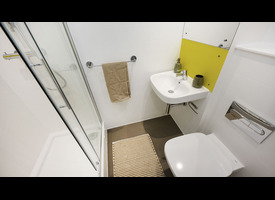 An ensuite shower with white hexagonal wall tiles, chrome fittings and a recessed yellow storage shelf.&rdquo;