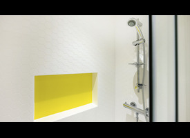 An ensuite shower with white hexagonal wall tiles, chrome fittings and a recessed yellow storage shelf.&rdquo;