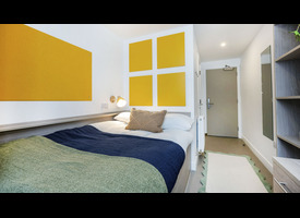 A modern student bedroom with a double bed, yellow accent panels, built-in shelving, study area and storage furniture.&rdquo;