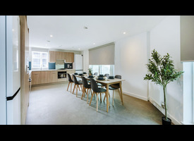A bright open-plan kitchen and dining area with modern wood-finish cabinets, a large dining table, and seating for eight.&rdquo;