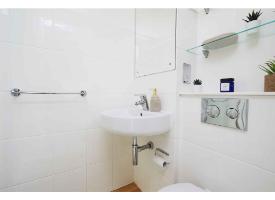A bathroom with a wash basin, wall mirror, floating glass shelf and white tiled walls.