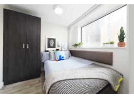 A bedroom with a double bed, dark wood wardrobe, large window and contemporary furnishings.