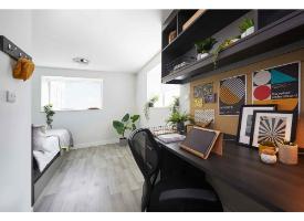 A modern room with a dedicated study desk, shelving, single bed, large window and modern wood-effect flooring.