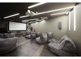 A cinema room with a large projector screen, surround sound speakers, beanbag seating and modern LED lighting.