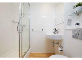 A modern ensuite bathroom with a glass shower enclosure, wash basin, wall mirror and wood-effect flooring.