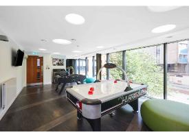 A communal games room with an air hockey table, table football, floor-to-ceiling windows and lounge seating.
