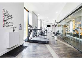 A modern gym with cardio and strength-training equipment, floor-to-ceiling windows, mirrored walls and contemporary finishes.