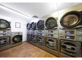 A shared laundry room with multiple commercial washing machines and dryers arranged along the walls.
