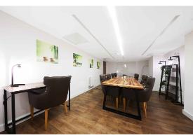 A study and meeting room with a large conference table, desk workspace, leather chairs, shelving and wood-effect flooring.