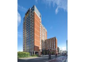 A modern student accommodation building with red brick and dark cladding faccediades, viewed from a city street with cyclists passing by.