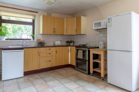 A kitchen/diner with a full-height fridge/freezer, an oven, kettle, toaster, and cupboard storage. Beneath the window there is a sink unit with an under-counter fridge.