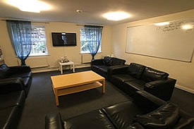 A room with five sofas laid out around a central coffee table. On the walls are mounted a television and a large whiteboard