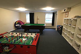 A room containing a table football game, a pool table, recycling bins and shelves