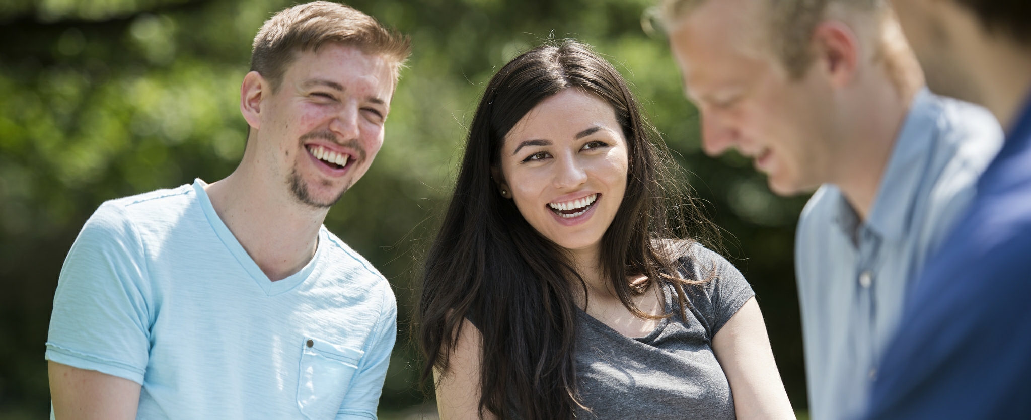 Two men and a woman laugh together outside in a garden.
