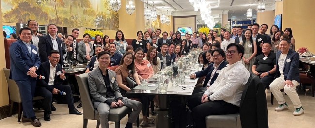 A large group of people looking at the camera smiling. They are gathered round long tables laid out for a meal