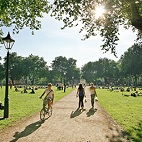 Queen's Square in the sun with people walking and cycling.