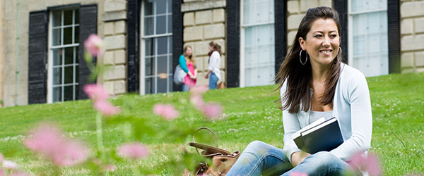 A female postgraduate student sitting on the grass outside a University building.