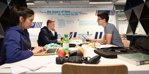 A woman and two men working on laptops at a table.