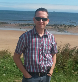 Photo of Natalio Krasnogor. He is pictured at a beach, wearing a plaid shirt, jeans and sunglasses.
