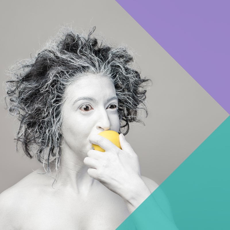 A mostly black and white photograph of a woman taking a bite out a yellow lemon