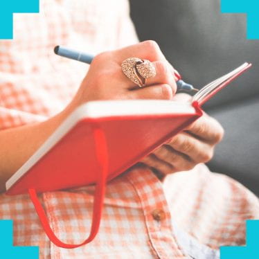 a close up photograph of somebodies hands as they write in a diary resting on their lap