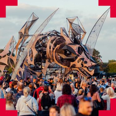 a crowd of people looking onto a 'life-size' abstract puppet of a dragon