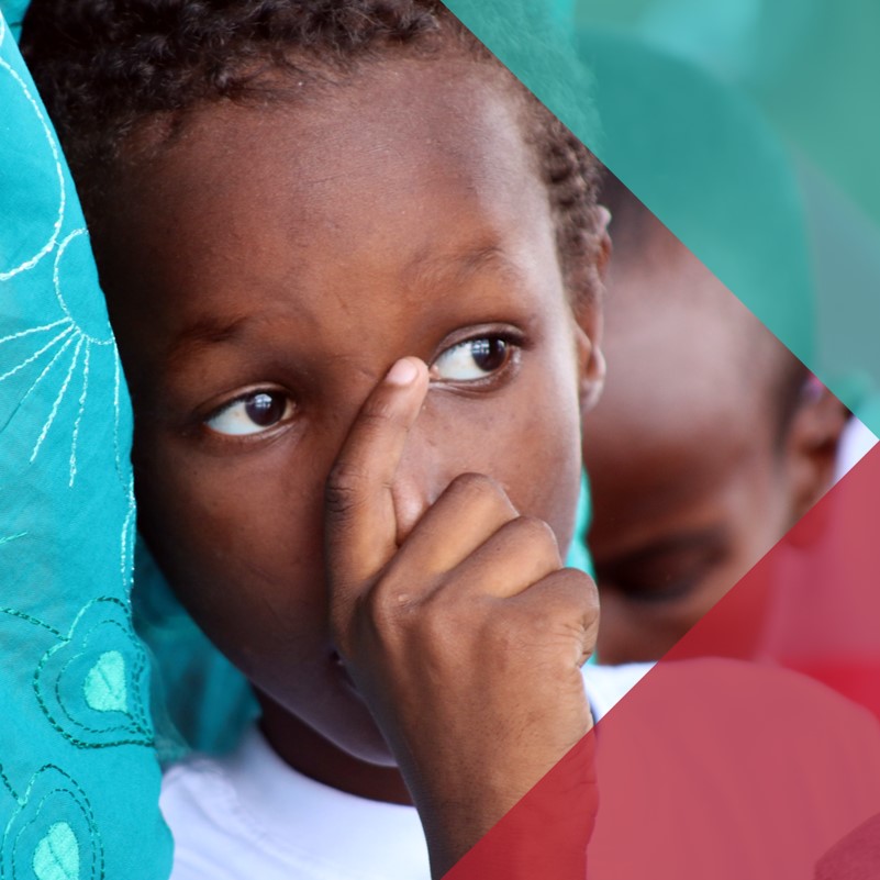 Young Somali boy stood next to his mother holding his hand in front of his face