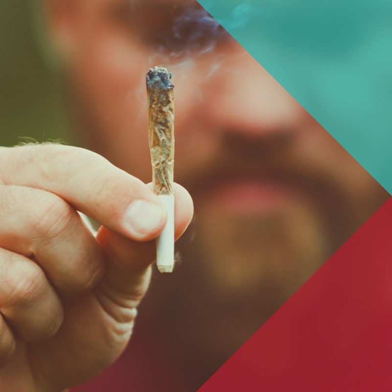 A photograph of a man holding a cannabis joint in front of his face to the camera