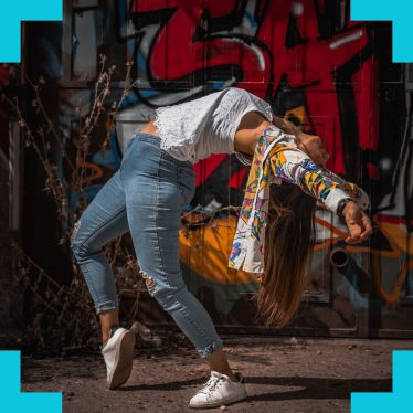 a woman in a dance pose in front of a wall with graffiti