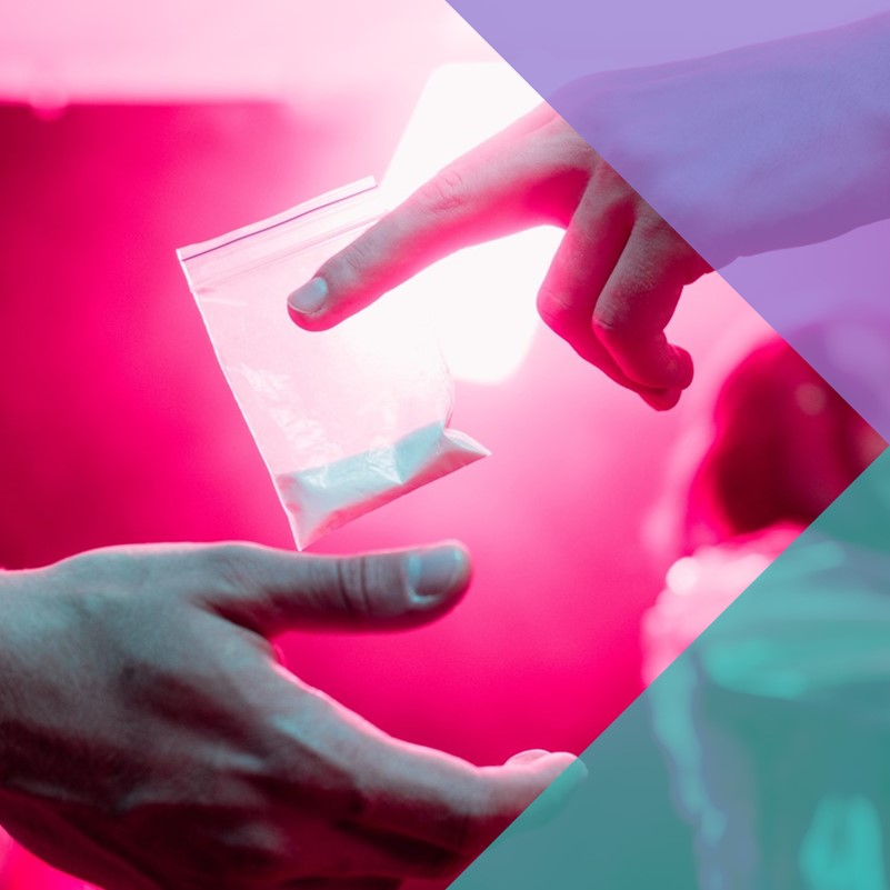 One hand passing a small plastic bag of drugs to another hand in a nightclub setting