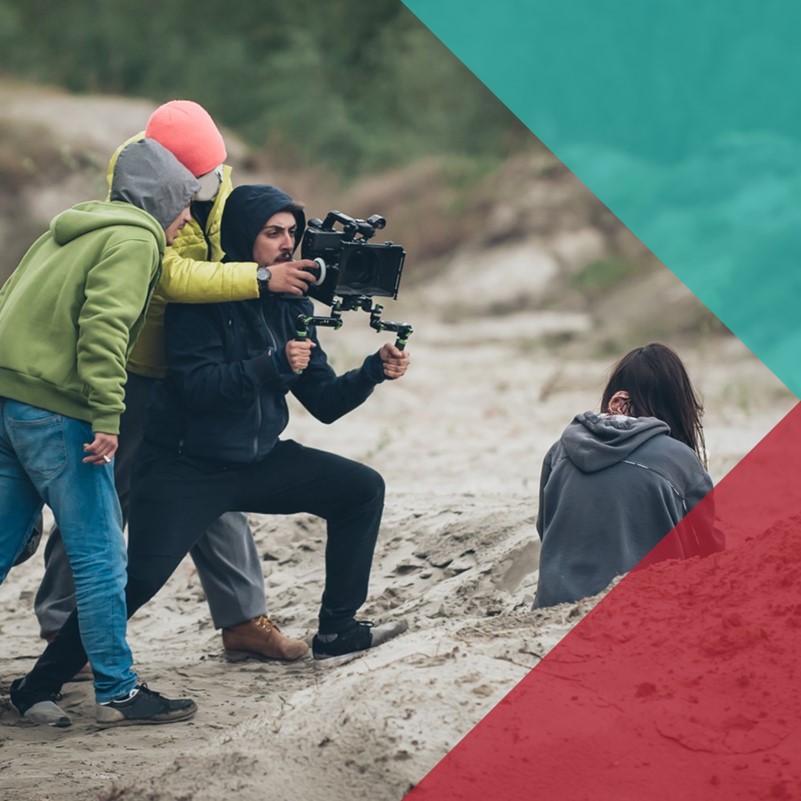 a small camera crew operating an industry film camera in an outdoor location, filming a young woman sat on the ground
