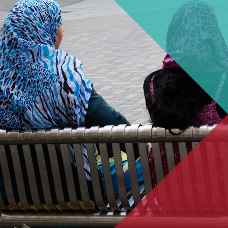 A photo of two woman sat on a bench wearing colourful and patterned head coverings