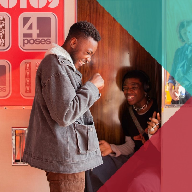 Two young black men laughing together in and outside a photobooth