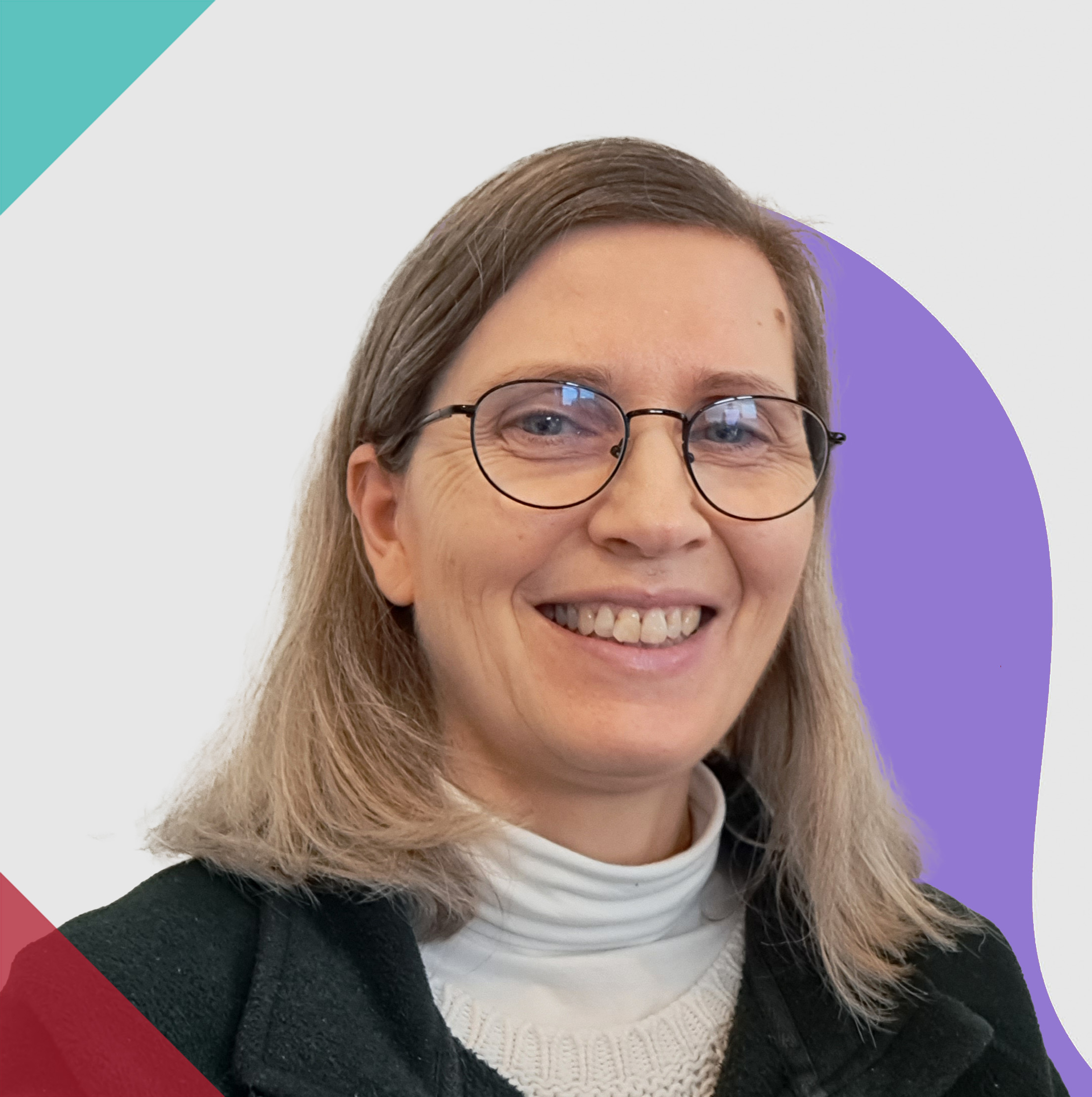a lady in her 50s with Shoulder length brown and grey hair, an open smile and glasses.