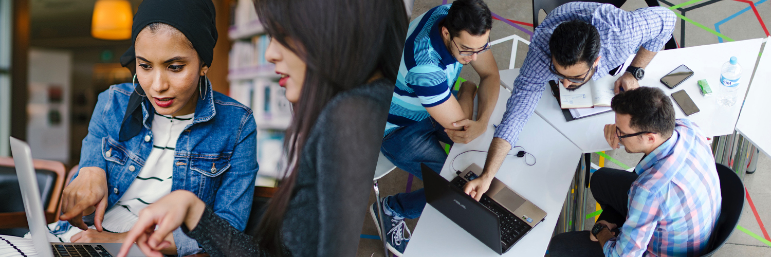 Two women sitting at a desk discussing something on a laptop alongside a group of men sitting in an office discussing something on a computer screen