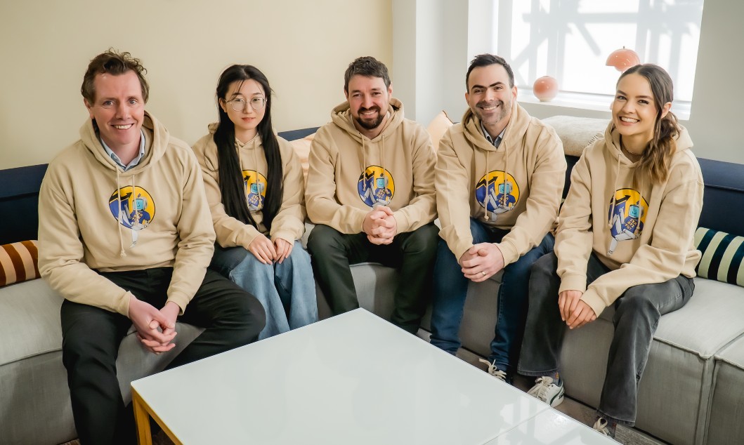 A team of people who work for Stratiphy sat on a sofa smiling at the camera. They are all wearing matching, Stratiphy branded hoodies.