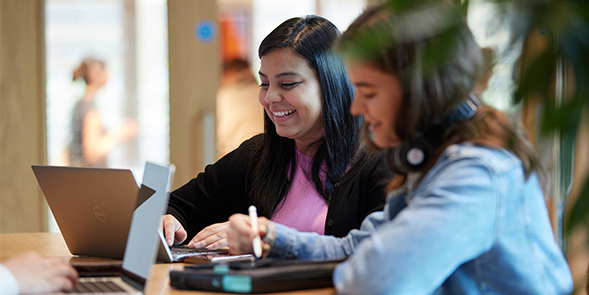 two students working on laptops on campus