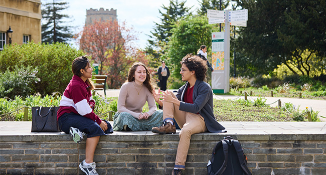 Three students sat on a stone wall talking with the Wills Memorial Building in the background