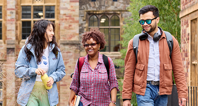 Three postgraduate students walking and talking outside a campus building